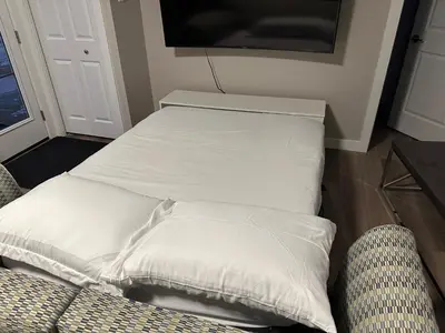 a bed with white pillows sitting next to a couch at Cozzy & Brand New Apartment, Near Banff Hwy in Calgary