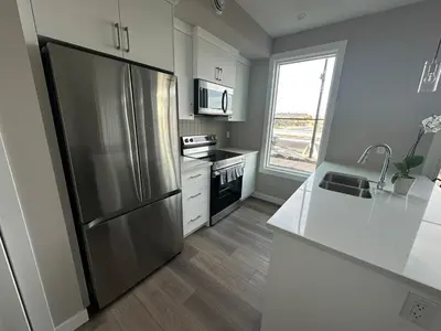 a kitchen with a stainless steel refrigerator and white cabinets at Cozzy & Brand New Apartment, Near Banff Hwy in Calgary
