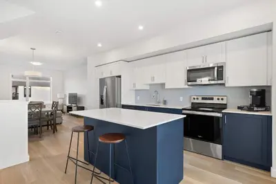 a kitchen with white cabinets and a blue island at Skyline Retreat Spacious 4BR Home with Balcony! in Calgary