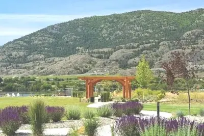 a wooden arch in a field with a mountain at Sandy beach Sauvignon cottage - Osoyoos escapade 3bd-2bt in Osoyoos