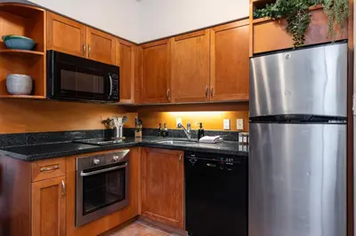 a kitchen with wooden cabinets and a stainless steel refrigerator at Village Penthouse w Views Pool and Hot Tub in Whistler