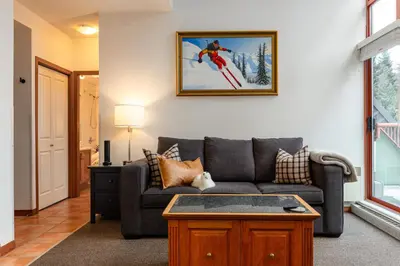 a living room with a couch and a picture of a skier at Village Penthouse w Views Pool and Hot Tub in Whistler