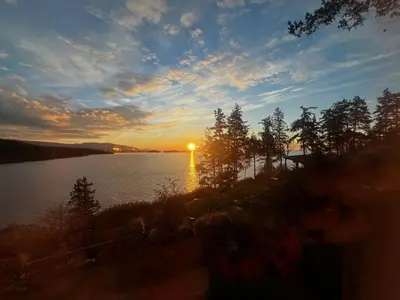 a sunset over a body of water with trees at Oceanfront Garden Suite - Stunning Views & Wildlife in Halfmoon Bay