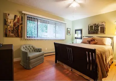 a bedroom with a bed and a chair and a window at Cole's Bay Vacation Retreat Petie's Cottage in YYJ