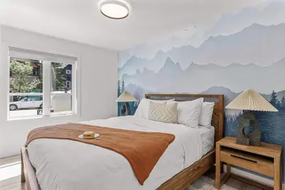 a bedroom with a bed with a mountain mural on the wall at Newly Built 2BR Mountain Escape in DT Canmore! in Canmore