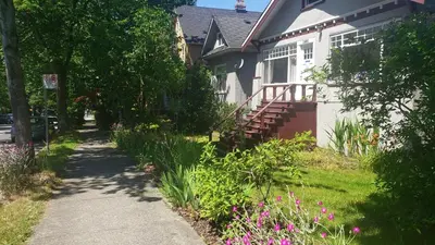 a house with a sidewalk next to a yard with flowers at Craftsman Home in popular East Village in Vancouver