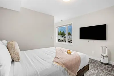 a white bedroom with a bed and a flat screen tv at Charming 2BR Haven in Canmore Near DT and Banff in Canmore