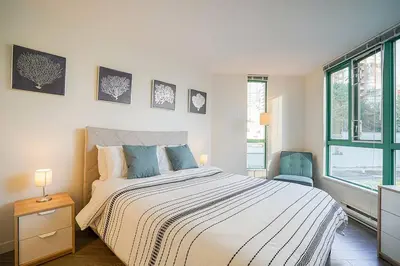 a white bedroom with a bed and a window at Yaletown Gorgeous Unit Steps from the Beach in Vancouver