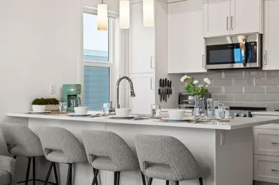 a kitchen with white cabinets and a counter with stools at Luxury Aspen 2BR Home with Double Garage Car Parking in Calgary