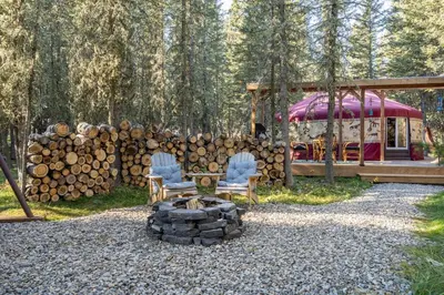 two chairs and a fire pit in front of a pile of logs at Shanti Yurt with private hot tub in Bragg Creek in Bragg Creek
