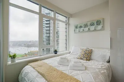 a white bed in a room with a large window at Modern Downtown Apartment with Water Views in Vancouver