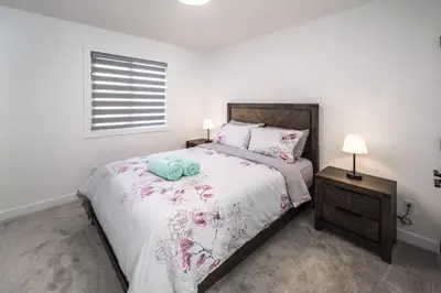 a white bedroom with a large bed with flowers on it at Group Stay, Sleeps 16! Near Downtown - 6BR Full Duplex, 2 Kitchens! FREE Banff Pass in Calgary