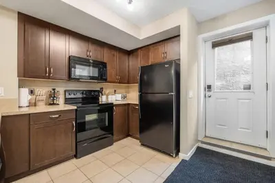 a kitchen with wooden cabinets and a black refrigerator at The Grande 1BD 1BA - Full Kitchen Guest Suite in Calgary