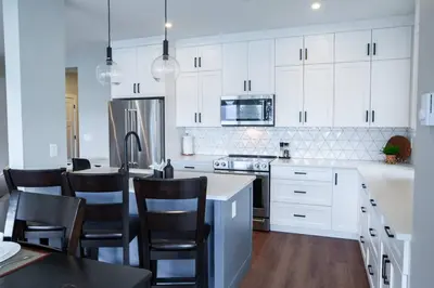 a kitchen with white cabinets and a table and chairs at 2 Bedroom with Lake and Mtn Views in Harrison Hot Springs