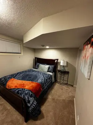 a bedroom with a bed with an orange blanket at Cozy and Spacious Basement in Chestermere
