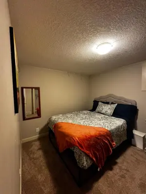 a bedroom with a bed with an orange blanket at Cozy and Spacious Basement in Chestermere