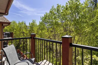 a balcony with a chair and a fence with trees at Creekside Downtown 2 Bedroom Condo managed by Little Sister Getaways in Canmore