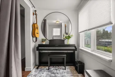 a mirror above a piano in a room with a guitar at Bluebird 3 Bedroom Home in the Heart of Drumheller in Drumheller