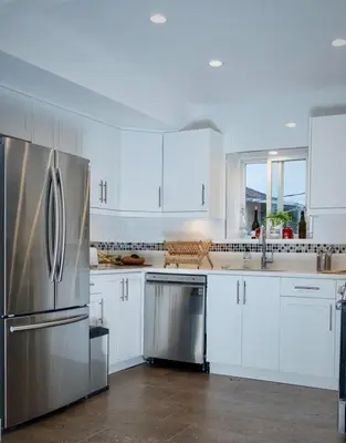 a kitchen with white cabinets and a stainless steel refrigerator at Beautiful Vancouver Cedar Cottage House in Vancouver