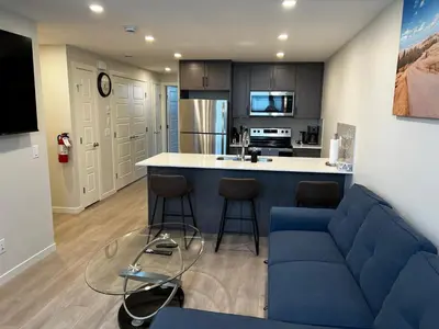 a living room with a blue couch and a kitchen at The Oasis-A New 1 bed suite in Livingston Calgary close to the Airport in Calgary