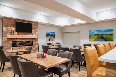 a waiting room with tables and chairs and a fireplace at Canalta Cochrane in Cochrane