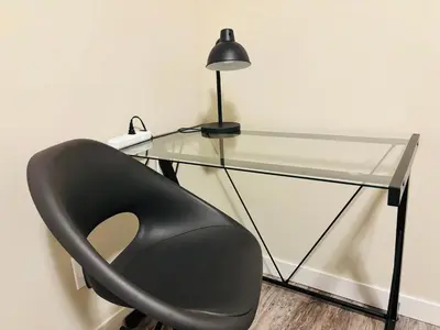 a glass desk with a black chair and a lamp at Main Floor 1 Bedroom Suite with Parking in Calgary