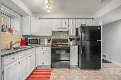 a kitchen with white cabinets and a black refrigerator at Modern 3 Bedroom Suite Near Downtown & Stampede Grounds in Calgary