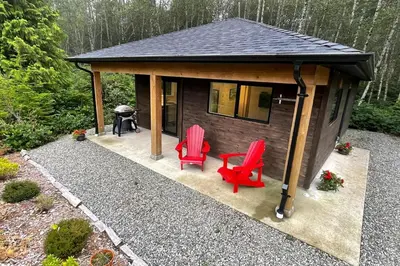 a small cabin with two red chairs and a grill at Tidal Retreat Cabin in Tofino