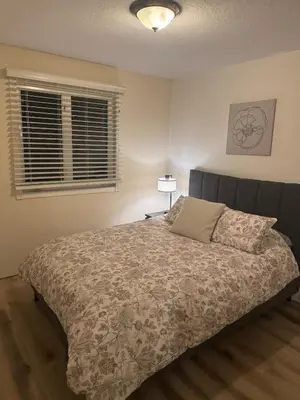 a bedroom with a bed and a lamp and two windows at Alpenglow Oasis in Hinton