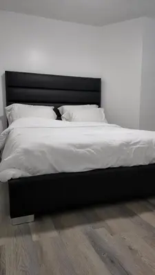 a bed with a black frame and white sheets and pillows at 2bedroom, 2bed day light Suite in a nice and secured neighborhood in Prince George