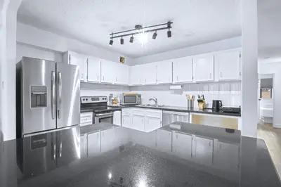 a kitchen with white cabinets and a stainless steel refrigerator at Stylish Suite at Stampede w Free Parking and AC in Calgary