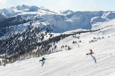 a group of people skiing down a snow covered slope at 2BR and Loft in Wildwood Lodge, Mountain Views, Close to Ski Hill, Common Hot Tub, Fireplace, Parking in Whistler