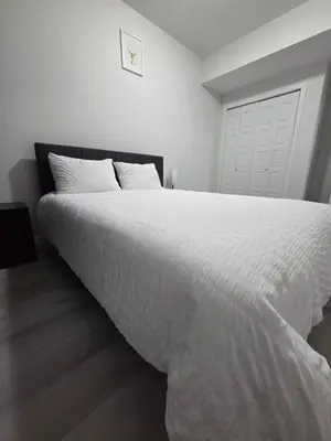 a bedroom with a large bed with white sheets at Elegant & Cozy 2 Bdrm Basement suite near WEM in Edmonton