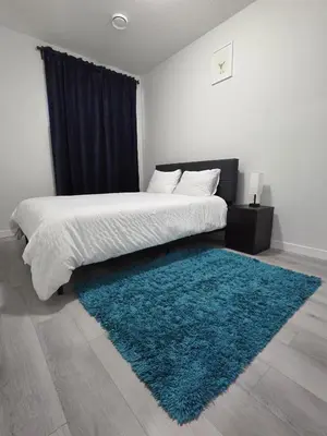 a bedroom with a large bed with a blue rug at Elegant & Cozy 2 Bdrm Basement suite near WEM in Edmonton