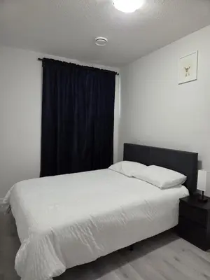 a bedroom with a white bed with a black window at Elegant & Cozy 2 Bdrm Basement suite near WEM in Edmonton