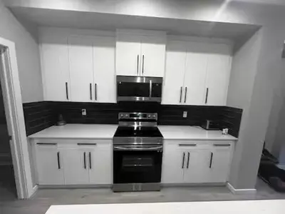 a kitchen with white cabinets and a black stove at Brand New Bedroom in Keswick B in Edmonton