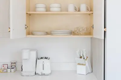 a kitchen with white cabinets and white dishes on a shelf at Brass Apple Cottage in Campbell River