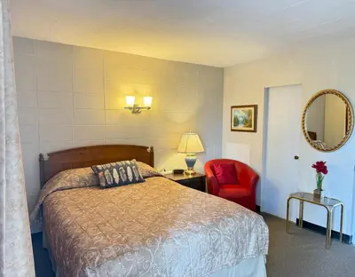 a hotel room with a bed and a red chair at Athabasca Hillside Motel in Athabasca