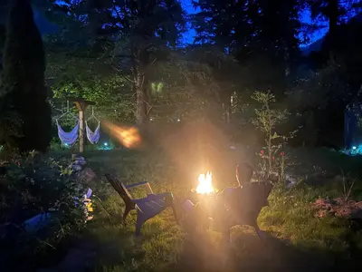 a man sitting around a fire in a garden at night at Posada Nordica - a chic, tranquil mountainview suite in Hope