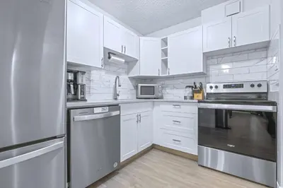 a kitchen with white cabinets and stainless steel appliances at Cozy & Spacious 2BR at Stampede w Parking and AC in Calgary