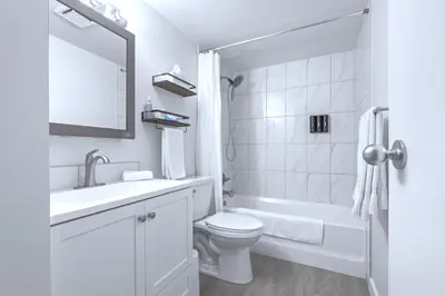 a white bathroom with a toilet and a sink at Cozy & Spacious 2BR at Stampede w Parking and AC in Calgary