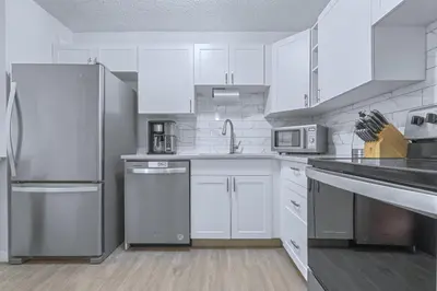 a kitchen with white cabinets and stainless steel appliances at Cozy & Spacious 2BR at Stampede w Parking and AC in Calgary