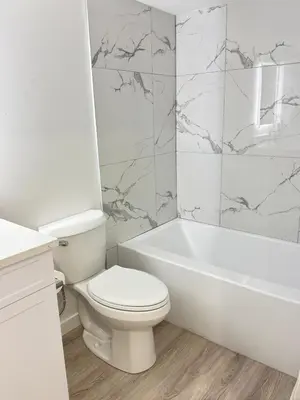 a white bathroom with a toilet and a bath tub at Modern Comfort in West Edmonton in Edmonton