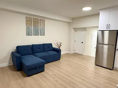 a living room with a blue couch and a refrigerator at Sunny White Rock 2BR, Steps to Sand, Brand New Stay in White Rock