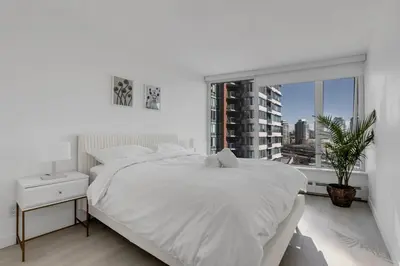 a white bedroom with a large bed and a window at Bright 3BR Downtown Vancouver Condo w Pool & Gym in Vancouver