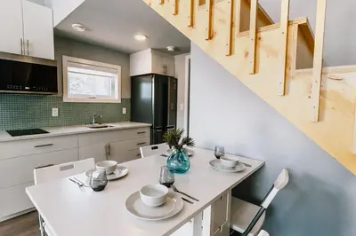 a kitchen with a white table with chairs and a staircase at Eagle - Cozy tiny home with mountain views in Nordegg