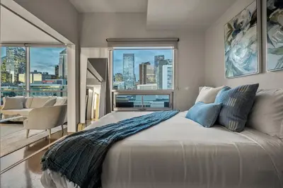 a bedroom with a large bed with a view of a city at The Chic Downtown Residence | Luxe + Free Parking in Calgary