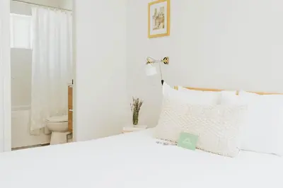 a white bedroom with a white bed and a toilet at Naramata Courtyard Suites in Naramata