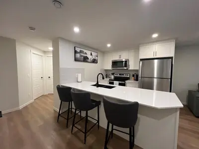 a kitchen with a white counter top and bar stools at Deluxe 2-Bedroom Getaway Near Calgary Airport Sleeps Up to 6 in Calgary