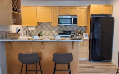 a kitchen with a black refrigerator and two bar stools at Modern 1br Apt, Up to 4 people, Steps to 17th Ave, Downtown & Stampede in Calgary